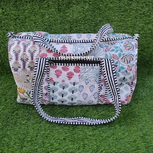 Puede incluir: Una bolsa de lona de algodón blanco con parches, con correas a rayas blancas y negras. La bolsa tiene cierre de cremallera y está decorada con coloridos patrones florales.