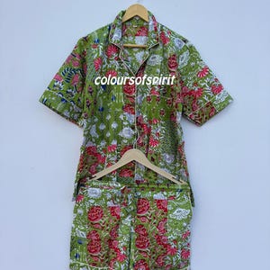 Peut inclure: Ensemble de pyjama à imprimé floral vert, composé d'un haut à manches courtes et d'un short assorti. L'ensemble présente une bordure blanche et le texte "coloursofspirit". Le motif floral comprend des fleurs rouges et blanches sur fond vert.