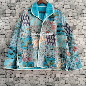 May include: A long-sleeve jacket featuring a patchwork design with various floral and paisley patterns in shades of blue, pink, and orange. The garment has a wide collar, a light blue trim, and visible white stitching throughout the fabric.