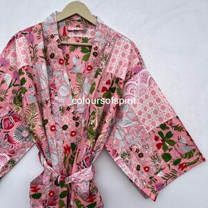 Könnte beinhalten: Ein rosa Bademantel mit floralem Muster und passendem Gürtel. Der Bademantel hat ein Patchwork-Design mit verschiedenen floralen Mustern in Rosa-, Rot-, Grün- und Weißtönen. Der Text "coloursofspirit" ist sichtbar.