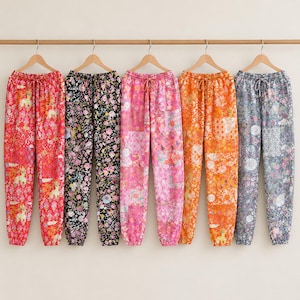 May include: Five pairs of drawstring lounge trousers hanging on wooden hangers. The trousers feature various floral and geometric patterns in red, black, pink, orange, and blue colourways, each with an elasticated waistband and cuffed ankles.