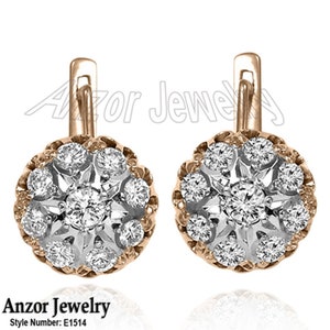 Pode incluir: Um par de brincos dourados com um design floral. Cada brinco apresenta um conjunto de pedras preciosas redondas e transparentes, rodeadas por uma moldura dourada. Os brincos têm um fecho de pressão. A marca "Anzor Jewelry" e o número do estilo "E1514" são visíveis.