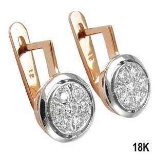 Pode incluir: Um par de brincos de ouro e prata com um centro redondo cravejado de diamantes. Os brincos têm um fecho de pressão e o texto "18K" é visível.