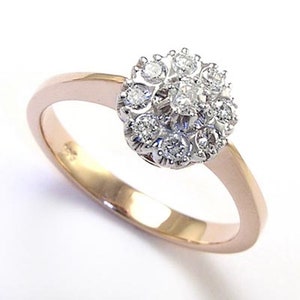 Pode incluir: Um anel de ouro e diamantes com um padrão floral. O anel tem uma banda de ouro rosa e uma cravação em ouro branco. O anel está sobre um fundo branco. O design do anel lembra uma flor.