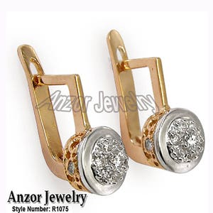 Pode incluir: Brincos de ouro e prata com um grupo de pequenas pedras brilhantes em uma configuração redonda. Os brincos têm um fecho de alavanca. A marca "Anzor Jewelry" e o número do estilo "R1075" são visíveis.
