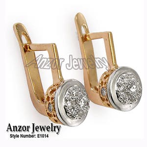 Pode incluir: Um par de brincos dourados com fecho de alavanca e uma cravação redonda em metal branco incrustada com pequenas pedras brilhantes. Os brincos têm um design de duas cores e estão rotulados como "Anzor Jewelry", número de estilo E1014.