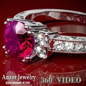 May include: A silver ring with a large, deep red ruby gemstone surrounded by smaller, clear diamonds. The band is engraved with the words "Anzor Jewelry" and the style number "R1386". 360° VIDEO.