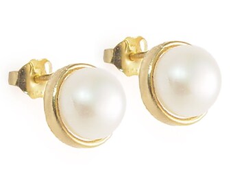 May include: A pair of gold stud earrings, each featuring a large, round, white pearl. The pearls are set in a gold bezel setting. The earrings have a classic and elegant design, suitable for various occasions.