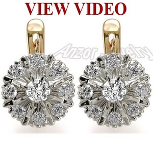 Pode incluir: Um par de brincos de prata e ouro com um design floral. Cada brinco apresenta uma pedra preciosa central, redonda e transparente, rodeada por pedras preciosas menores, criando um efeito de explosão estelar. A parte superior dos brincos é dourada, e o texto "VIEW VIDEO" é visível.