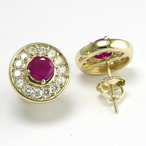 Op de afbeelding: Een paar gouden oorbellen met een rode robijn-edelsteen omringd door een halo van kleinere witte edelstenen.