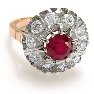 Puede incluir: Un anillo de rubí rojo con un halo de pequeños diamantes engastados en oro blanco. La banda es de oro rosa.