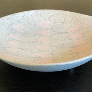 May include: A light blue ceramic serving bowl with a pink and white geometric pattern. The bowl has a unique shape with a pointed end.
