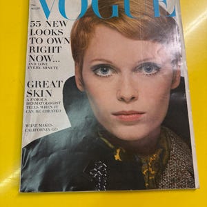 Peut inclure: Une couverture du magazine Vogue vintage du 15 août. La couverture présente une femme aux cheveux courts, brun-roux et aux yeux bleus perçants. Le titre du magazine, "VOGUE", est en grandes lettres turquoise. Le texte comprend "55 NOUVEAUX LOOKS À POSSÉDER MAINTENANT..." et "GREAT SKIN."
