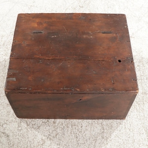 May include: A rectangular wooden box with a hinged lid. The box is made from dark brown wooden planks, showing visible grain and knots. The box appears aged, with signs of wear and tear.