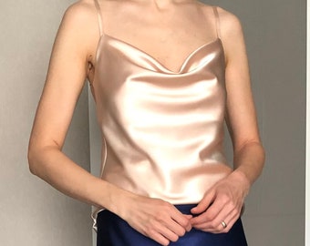 May include: A silky, blush-colored tank top with a cowl neck and thin straps. The top is paired with a dark blue satin skirt.
