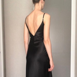 Puede incluir: Un vestido maxi de satén negro con un profundo escote en V en la espalda y tirantes finos.