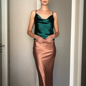 Puede incluir: Una mujer lleva una blusa de satén verde y una falda de satén marrón. La falda es de largo midi y tiene una ligera forma de A.