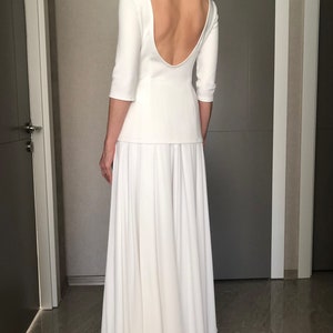 May include: A white maxi dress with a low back and three-quarter sleeves. The dress has a fitted bodice and a flowing skirt.