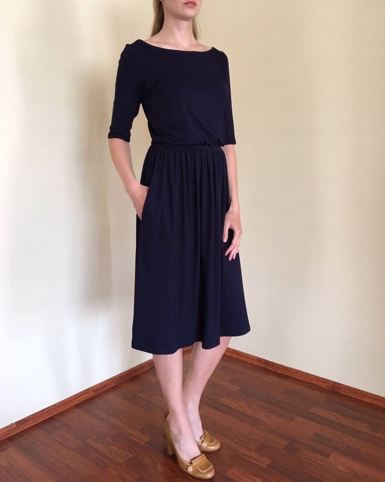 Op de afbeelding: Een donkerblauwe midi-jurk met een boot halslijn en 3/4 mouwen. De jurk heeft een geplooide taille en een licht uitlopende rok.