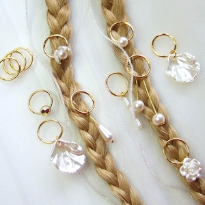 May include: Braided blonde hair adorned with gold rings, pearl accents, and shell-shaped charms. A collection of hair accessories for a stylish look. The accessories include small gold rings and pearl and shell charms.