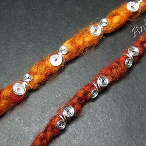 Könnte beinhalten: Zwei Strähnen rot-orangen geflochtenen Haars mit silbernen Metallringen. Die Ringe sind entlang der Haarsträhnen verteilt.