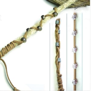 May include: A close-up of a brown leather cord wrapped around a blonde synthetic dreadlock with silver and gold metal beads. The cord is tied off with a knot and has a long tail. The dreadlock is also decorated with silver metal beads. The image shows a close-up of the dreadlock and the cord, with the background blurred.