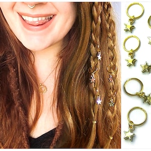 Op de afbeelding: Gouden haarringen met stervormige bedels. De ringen zijn ontworpen om dreadlocks of vlechten op hun plaats te houden. De bedels zijn klein en delicaat en voegen een vleugje glans toe aan het haar.