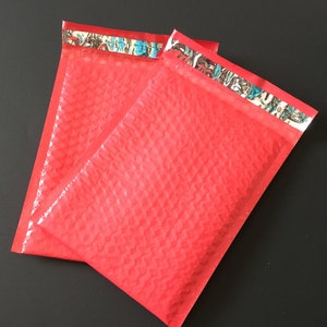 May include: Two red bubble mailers with a patterned design on the flap. The mailers are made of a soft, flexible material and are designed to protect items during shipping.