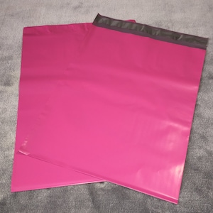 Puede incluir: Dos sobres de envío de color rosa con una franja negra en la parte superior.