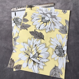 May include: A yellow poly mailer with a white and gray floral pattern. The flowers are stylized and resemble daisies. The mailer is made of a durable plastic material and is perfect for shipping small items.