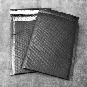 Könnte beinhalten: Zwei schwarze gepolsterte Versandtaschen mit Luftpolsterfolie. Die Umschläge sind versiegelt und versandbereit.