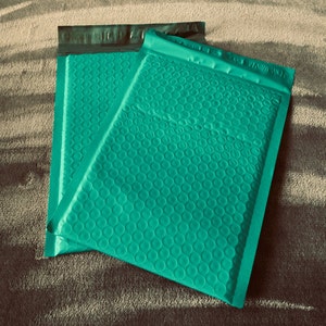 May include: Two green bubble mailers, one on top of the other. The mailers are made of a soft, padded material with a textured surface.