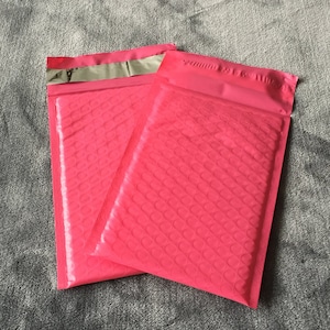 May include: Two pink padded mailing envelopes with a silver strip along the top edge.