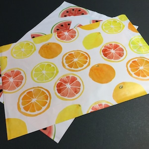 May include: Two white mailing envelopes with a repeating pattern of colorful fruit slices. One envelope has a watermelon pattern, the other has a pattern of lemons, oranges, and grapefruits.