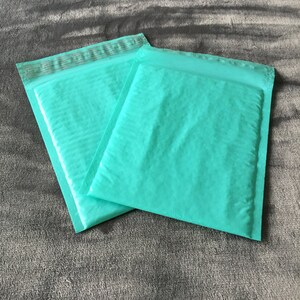 Könnte beinhalten: Zwei gepolsterte Umschläge in Türkisblau, einer auf dem anderen.