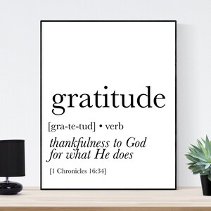 May include: A black and white printable wall art design with the word 'gratitude' in bold font. The definition of the word is provided in brackets: [gra-te-tud] • verb thankfulness to God for what He does [1 Chronicles 16:34]
