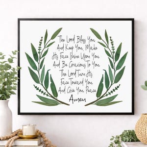 May include: A framed print with the text "The Lord Bless You" surrounded by a green leaf wreath. The text is in black script on a white background. The frame is black.