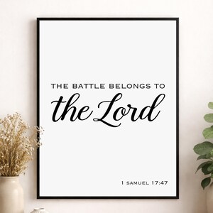 以下が含まれることがあります： 白い背景に黒い文字で「THE BATTLE BELONGS TO the Lord」、下部に「1 SAMUEL 17:47」と記された額装されたウォールアートプリント。プリントは細い黒いフレームに収められており、すっきりとしたコントラストの高いデザインが特徴です。