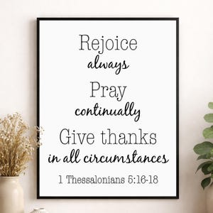 May include: A framed print with a white background and black text. The text reads "Rejoice always, Pray continually, Give thanks in all circumstances" and "1 Thessalonians 5:16-18". The frame is black.