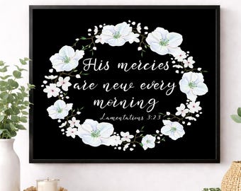 May include: A rectangular black wall art print featuring a white floral wreath surrounding the white text "His mercies are new every morning" and "Lamentations 3:23". The print is enclosed in a thin black frame, showcasing white blossoms.