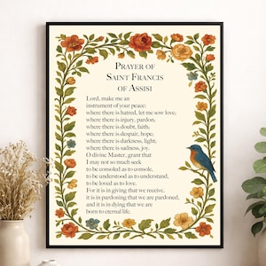 May include: A framed wall art print featuring the Prayer of Saint Francis of Assisi in black serif text on a cream background, surrounded by a decorative border of green vines, orange and yellow flowers, and a small blue bird on a branch.