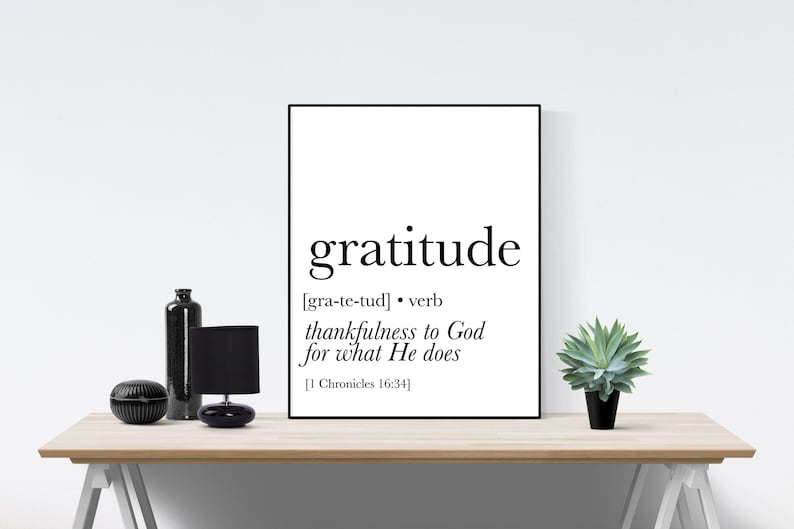 May include: A black and white printable wall art design with the word 'gratitude' in bold font. The definition of the word is provided in brackets: [gra-te-tud] • verb thankfulness to God for what He does [1 Chronicles 16:34]