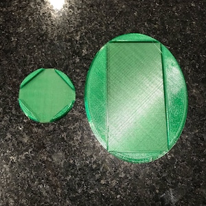May include: Two green plastic circular coasters. The larger coaster is slightly raised around the edges and has a rectangular shape in the center. The smaller coaster is round with a slightly raised edge.