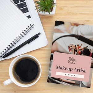 Peut inclure: Un agenda rose et blanc avec le texte "Makeup Artist Planner" sur la couverture. La couverture pr&eacute;sente &eacute;galement une illustration en noir et blanc d'une trousse de maquillage avec des pinceaux.