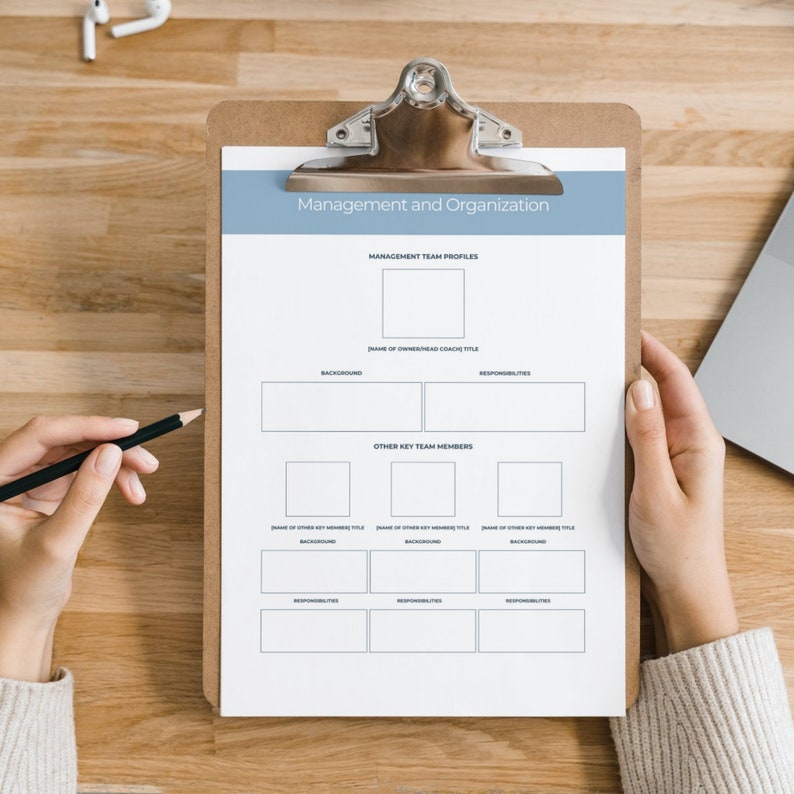 May include: A white clipboard with a blue header that reads "Management and Organization". The clipboard has a checklist for a management team, including sections for "Management Team Profiles", "Other Key Team Members", "Background", and "Responsibilities".