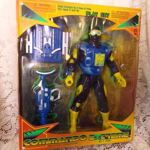 May include: A blue and yellow action figure toy with a blue and black backpack and a blue and green gun. The toy is packaged in a box with the words "Commando Extreme" on it.