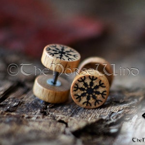 May include: Three wooden ear gauges featuring a black snowflake design. The gauges are round and have a smooth, polished finish.