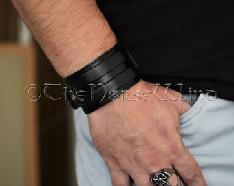 May include: A wide black leather cuff bracelet with a buckle closure. The bracelet is worn on a person's wrist.