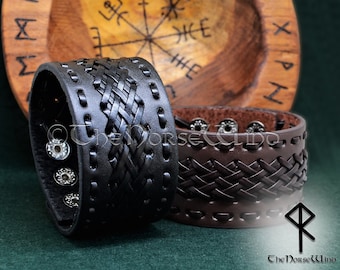 May include: Two leather bracelets with a braided design. The bracelet on the left is black and has silver studs. The bracelet on the right is brown. Both bracelets have a stitched edge.