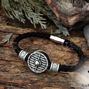 May include: Black leather bracelet with a silver shield charm and three silver bead accents. The bracelet has a magnetic clasp. The text "The Norse Wind" is visible in the image.